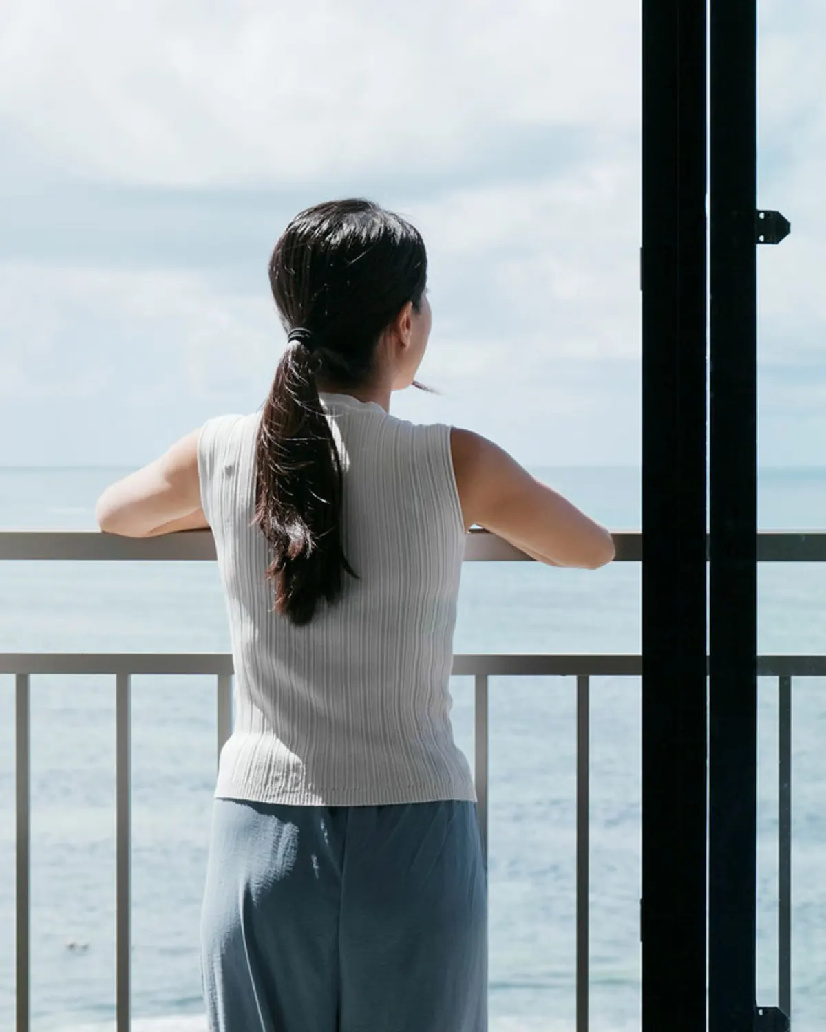 Woman overlooking the ocean from a sunny balcony