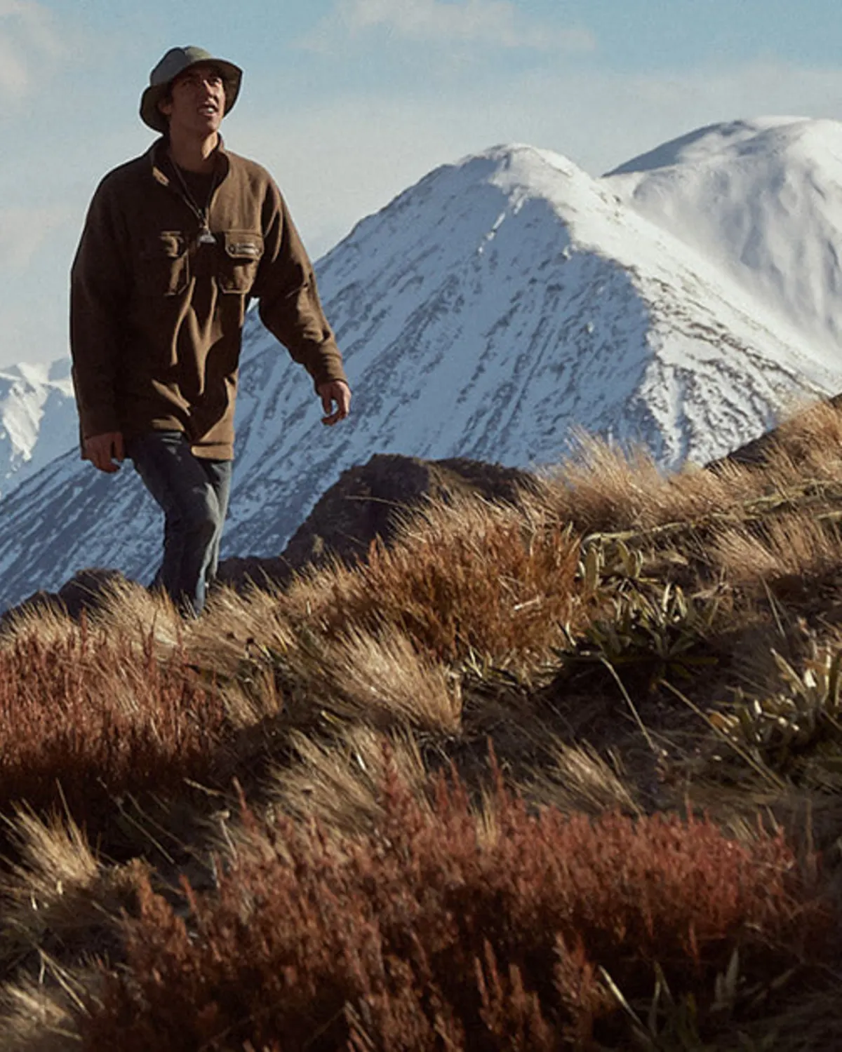 Hiker crossing alpine grassland beneath snow-covered mountains