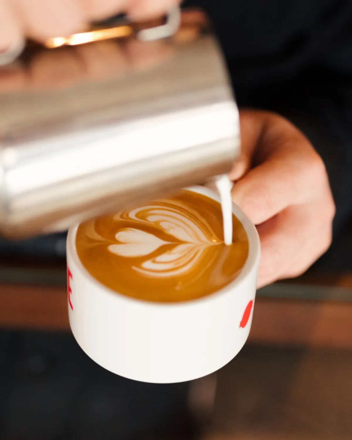 Barista pouring leaf-shaped latte art into a coffee cup