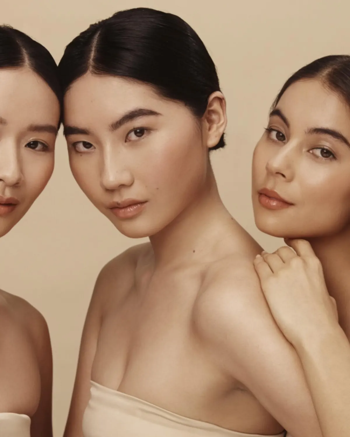 Three skincare models posing against a warm beige background