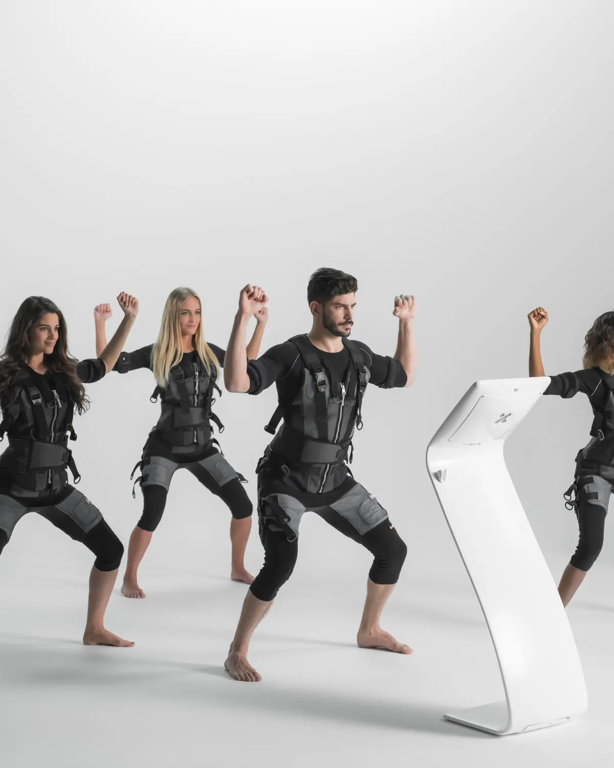 People training in EMS suits beside a fitness console