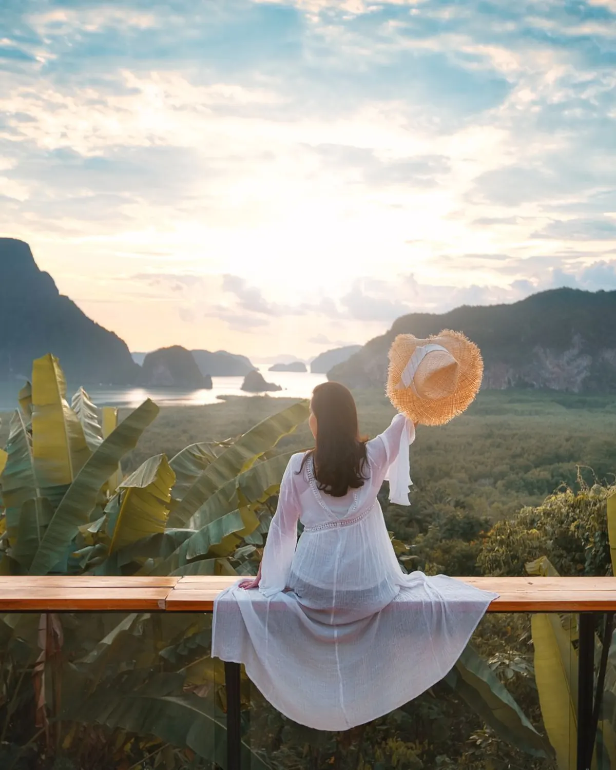 Traveller raises a sunhat over a tropical island valley