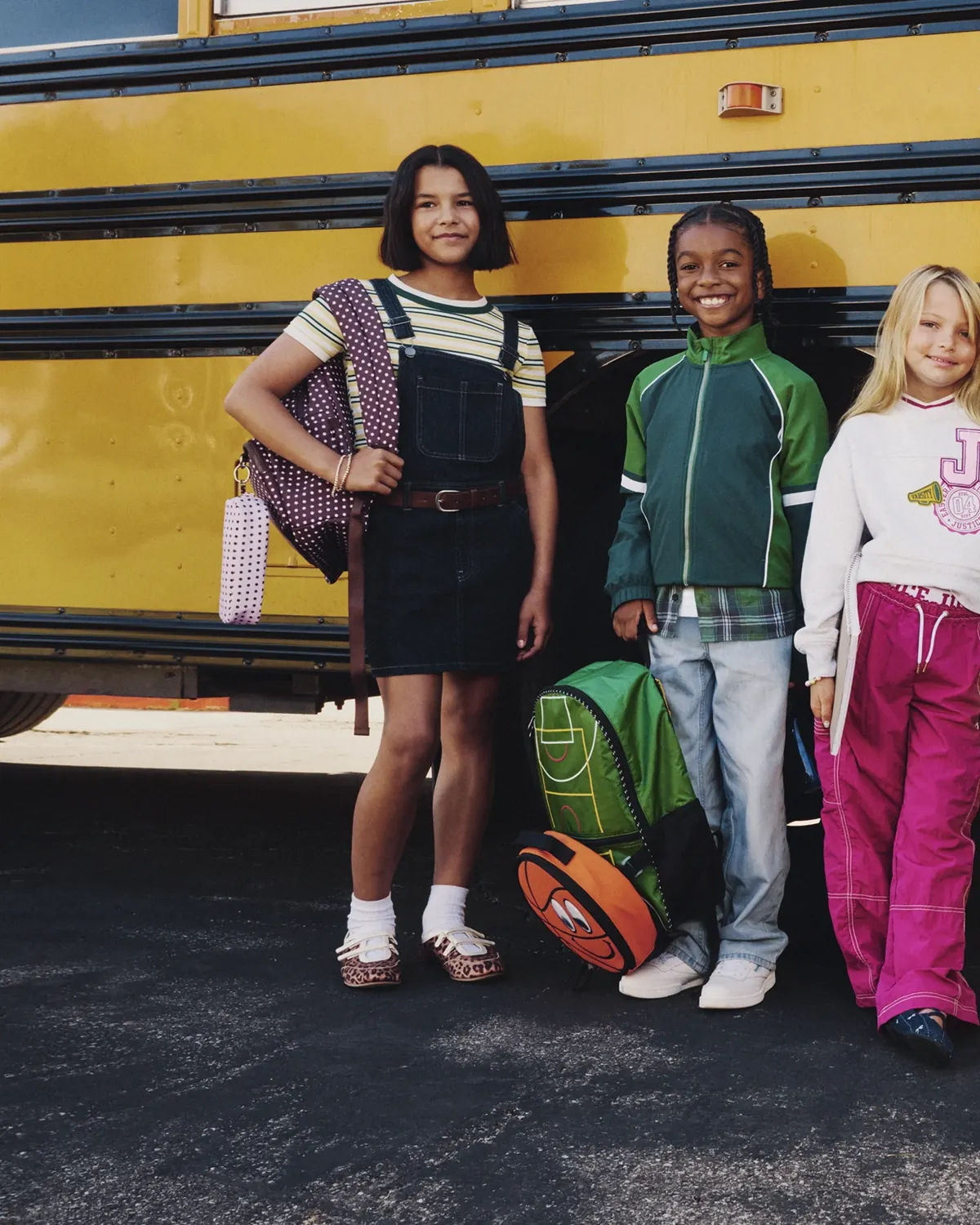 Three schoolchildren with backpacks beside a yellow school bus