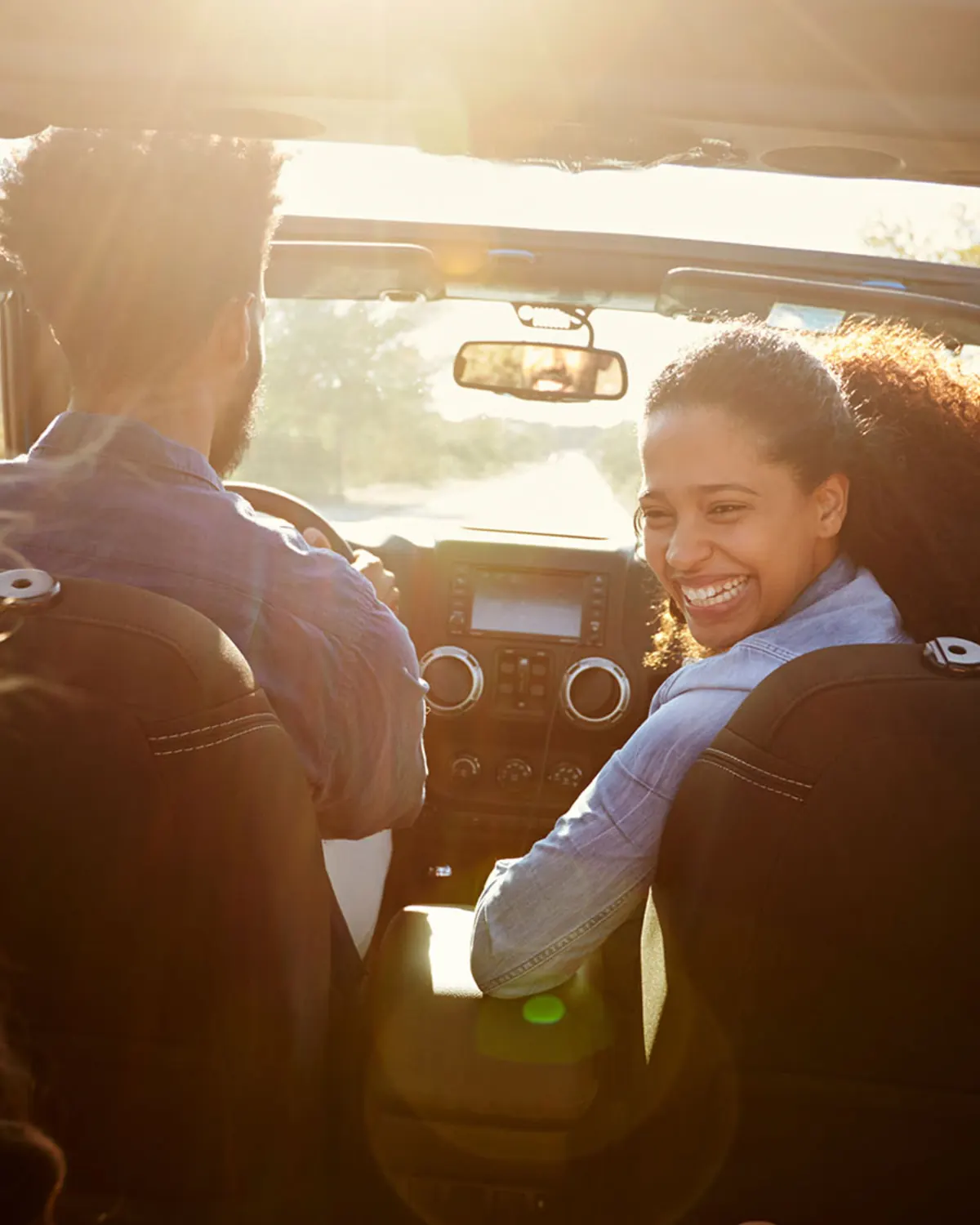 Smiling passenger looks back during a sunlit convertible road trip